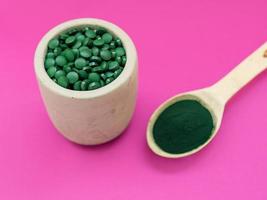 groene hawaiiaanse spirulina in poeder in houten lepel op roze achtergrond. superfood, gezonde levensstijl, concept voor gezonde supplementen foto