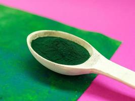 groene hawaiiaanse spirulina in poeder in houten lepel op roze achtergrond. superfood, gezonde levensstijl, concept voor gezonde supplementen foto