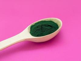 groene hawaiiaanse spirulina in poeder in houten lepel op roze achtergrond. superfood, gezonde levensstijl, concept voor gezonde supplementen foto