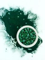 groene hawaiiaanse spirulina in eetlepels pillen op lichtlila achtergrond. superfood, gezonde levensstijl, concept voor gezonde supplementen foto