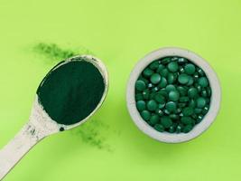 groene hawaiiaanse spirulina in eetlepels pillen en poeder op lichtgroene achtergrond. superfood, gezonde levensstijl, concept voor gezonde supplementen foto