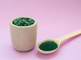 groene hawaiiaanse spirulina in eetlepels pillen en poeder op lichtlila achtergrond. superfood, gezonde levensstijl, concept voor gezonde supplementen foto