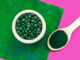 groene hawaiiaanse spirulina in eetlepels pillen en poeder op lichtlila achtergrond. superfood, gezonde levensstijl, concept voor gezonde supplementen foto