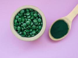 groene hawaiiaanse spirulina in eetlepels pillen en poeder op lichtlila achtergrond. superfood, gezonde levensstijl, concept voor gezonde supplementen foto