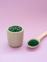 groene hawaiiaanse spirulina in eetlepels pillen en poeder op lichtlila achtergrond. superfood, gezonde levensstijl, concept voor gezonde supplementen foto