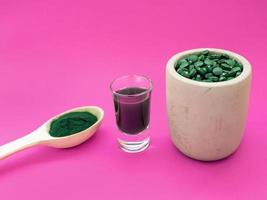 vloeibare spirulina groene drank in cocktailglas en spirulina pillen op roze achtergrond. superfood, gezonde levensstijl, concept voor gezonde supplementen foto