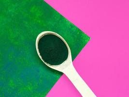 groene hawaiiaanse spirulina in poeder in houten lepel op roze achtergrond. superfood, gezonde levensstijl, concept voor gezonde supplementen foto