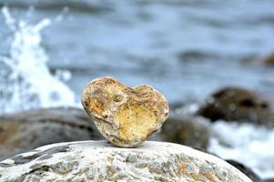 hartvorm steen tegen de achtergrond van het strand. zomer zonnige dag. liefde, huwelijk en valentijnsdag concept. mooie en interessante stenen vinden. strandvakantie foto