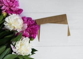 uitnodigingskaart, ambachtelijke envelop en roze pioenrozen foto