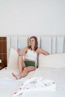 vrouw zittend op het bed in hotelkamer sms'en op mobiele telefoon foto