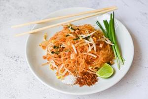 Thais eten gebakken noedels Thaise stijl met garnalen taugé en garnituur pinda's chili poeder suiker citroen limoen, roerbak noedels pad thai op bord geserveerd op de eettafel eten - bovenaanzicht foto
