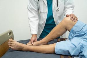 Aziatische arts fysiotherapeut onderzoekt, masseert en behandeling knie en been van senior patiënt in orthopedist medische kliniek verpleegster ziekenhuis. foto