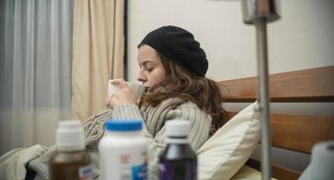 Spaanse vrouw die alleen in haar bed ligt, goed ingepakt, ziek van de griep, een kopje thee aan het drinken foto
