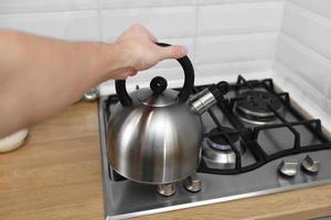 man hand met metalen waterkoker in de keuken. waterkoker heet water gebruiken om dranken zoals thee, koffie, melkpoeder of andere te koken. foto