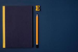bovenaanzicht omslag blauw notitieboekje met geel potlood en notitieblok op marineblauwe werktafel foto