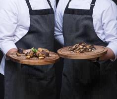 twee obers serveren een vleesgerecht op een houten dienblad foto