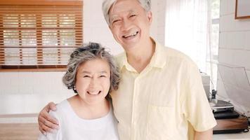 Aziatisch bejaarde echtpaar voelt zich gelukkig glimlachend en kijkt naar de camera terwijl ze ontspannen in de woonkamer thuis. genieten van tijd levensstijl senior familie thuis concept. portret camera kijken. foto