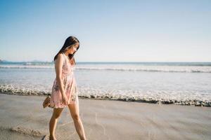 jonge Aziatische vrouw lopen op het strand. mooie vrouw gelukkig ontspannen wandelen op het strand in de buurt van de zee bij zonsondergang in de avond. levensstijl vrouwen reizen op strand concept. foto
