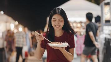 aziatische jonge vrouw reist in bangkok, thailand, mooie vrouw voelt zich gelukkig wandelen en eet pad thai op de khao san road. vrouwen reizen eten straatvoedsel in thailand concept. foto