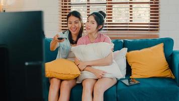 jonge azië lesbische lgbtq-vrouwen paar tv kijken thuis, aziatische minnaar vrouw gevoel gelukkig plezier lachen kijken televisieserie film samen terwijl liggend bank in woonkamer thuis concept. foto