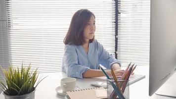 mooie jonge lachende Aziatische vrouw die op laptop werkt terwijl thuis in de werkruimte op kantoor. zakenvrouw werken vanuit huis via draagbare computer schrijven op toetsenbord. thuis genieten van tijd. foto
