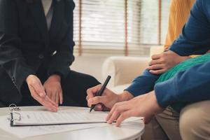 gelukkig jong Aziatisch stel en makelaar in onroerend goed. vrolijke jongeman ondertekent een aantal documenten terwijl hij samen met zijn vrouw aan het bureau zit. het kopen van nieuw onroerend goed. ondertekening contract in goede staat. foto