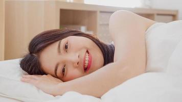 Aziatische vrouw die lacht liggend op bed in de slaapkamer, mooie Japanse vrouw die ontspantijd gebruikt na thuis wakker worden. levensstijl vrouwen die ontspannen tijd thuis concept gebruiken. foto