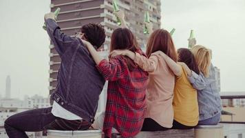 groep jonge Aziatische vrouwen en man mensen dansen en hun armen in de lucht opheffen op de muziek gespeeld door dj bij zonsondergang urban party op het dak. jonge Aziatische meisjes en jongensvrienden die rondhangen met drankjes foto