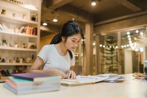 aziatische studentenvrouwen die boeken lezen in bibliotheek aan de universiteit. jong niet-gegradueerd meisje doet huiswerk, leest leerboek, studeert hard voor kennis op de collegebank op de overurennacht van de universiteitscampus. foto