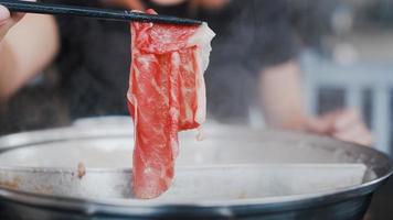 Aziatische vrouw die hete pot eet in Japans restaurant, jonge vrouw die gesneden rundvlees houdt door eetstokjes eet shabu tijdens de lunch. levensstijl vrouwen die voedselconcept eten. foto