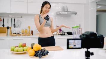 blogger sportieve aziatische vrouw met camera-opname hoe ze druivensapvideo maakt voor haar abonnee, vrouw gebruikt biologisch fruit om zelf thuis druivensap te maken. gezond voedselconcept. foto