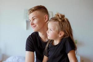 kaukasische broers en zussen - tienerjongen, broer en kleine meisjeszus in het moderne loft-interieur van de slaapkamer. typische gezinslevensstijl foto