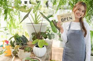 een vrouw die een boom verkoopt, houdt een welkom open bord in het groene huis. foto