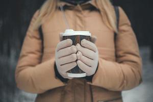 meisjeshanden in handschoenen houden een kop warme chocolademelk of koffie vast, getinte foto met kopieerruimte