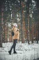 een jong meisje in winterkleren en met een medisch masker loopt in het winterbos. foto