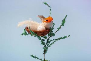 op een decoratieve boom, een nest met eieren en een kleine gele vogel op een blauwe close-up als achtergrond met exemplaarruimte foto