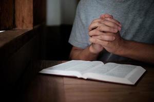 man met bijbel bidden, handen samengevouwen op haar bijbel op houten tafel. foto