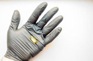 een gele capsule visolie in de hand in een zwarte medische handschoen op een witte achtergrond. hand met pillen op een witte achtergrond. foto
