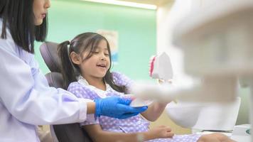 vrouwelijke tandarts die laat zien hoe je tanden poetst aan een klein meisje in de tandheelkundige kliniek, tandencontrole en gezond tandenconcept foto