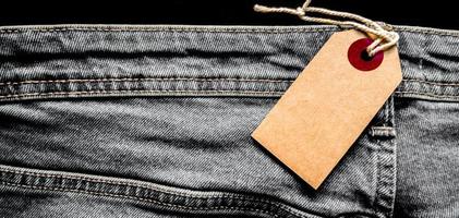 close-up jeans met lege kartonnen witte prijskaartje voor uw tekst. tag de witte mockup op de spijkerbroek. lege kopie ruimte. achtergrond, vakantieconcept. zwarte vrijdag - internationale dag van winkelen foto