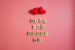 een paar rode hart- en letterwoorden wil je met me trouwen geïsoleerd op roze achtergrond. valentijnsdag, cadeau, bericht voor minnaar, wenskaart. liefdesconcept. foto
