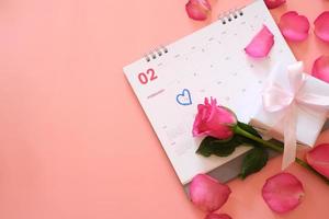 roze roos en een geschenkdoos op kalender met rozenblaadjes geïsoleerd op roze achtergrond met copyspace voor tekst. Valentijnsdag concept. planning planning agenda, evenement, organisator Valentijnsdag. foto