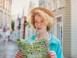 roodharige jonge vrouw reist over West-Europa en gebruikt een papieren kaart in een onbekende stad. reis foto. verloren in nieuwe stad foto