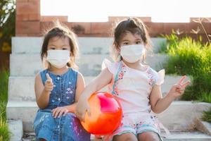 kinderen met een wit gezichtsmasker zitten op trappen. kind met rode bal. kind houdt vinger op naar v-teken. mooi meisje van 5 jaar oud. foto