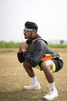 sport en gezond leven concept - Indiase jonge sportman met fitnesskleding die squats doet en traint op een veld. foto