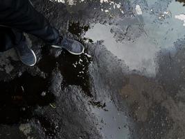 een foto van iemands voeten met trainingsbroek en schoenen op het asfalt op een weg met gaten en beschadigde weg zodat deze onder water staat