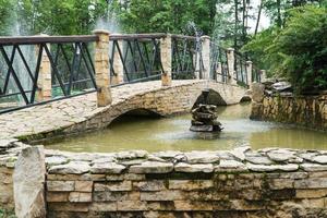 fontein en brug van stenen tegels in het park. een decoratieve vijver buiten foto