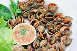 gepelde kokkels met zeevruchtensaus en groentesaladesla op plaatachtergrond, verse ruwe schelpdieren bloedkokkel oceaan gastronomische zeevruchten in het restaurant, zeeschelpenvoedsel foto