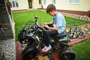 jongen in vierwielige atv quad met mobiele telefoon. foto