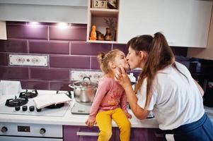 moeder met dochter koken in de keuken, gelukkige kindermomenten. moeder kust haar baby. foto